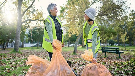 Das Foto zeigt zwei Frauen im Park, die sich freiwillig engagieren und Müll einsammeln.