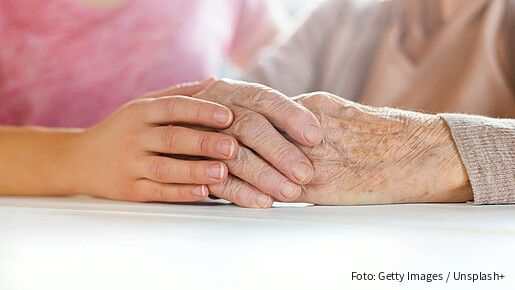 Foto einer jungen Hand, die eine ältere Hand umschließt.